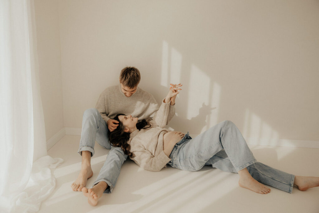 Babybauchfotografie Pärchen kuschelt zusammen auf Boden im Fotostudio